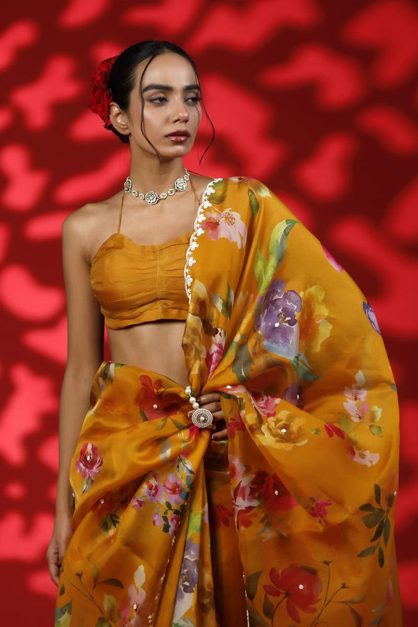 A woman wearing a mustard yellow party wear saree with floral prints against a red background