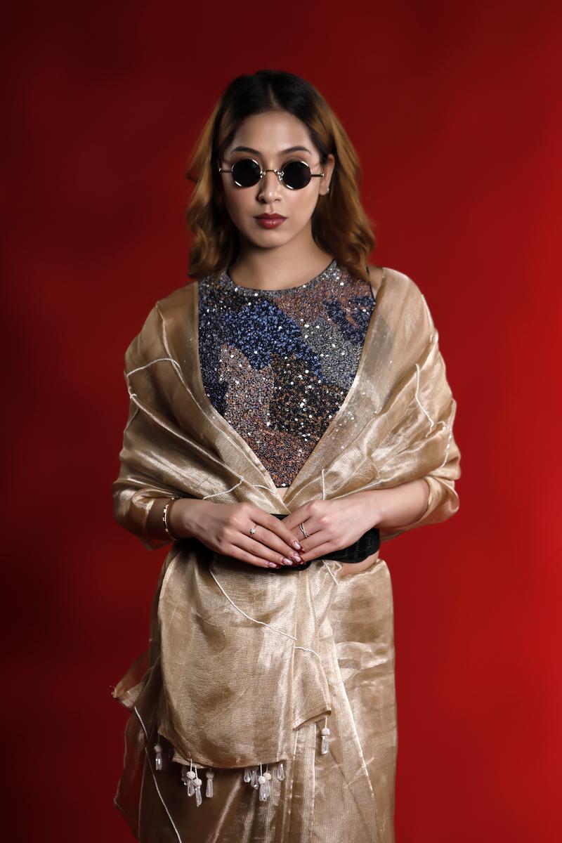 A woman wearing a golden party wear saree dress for a cocktail party looks against a red background