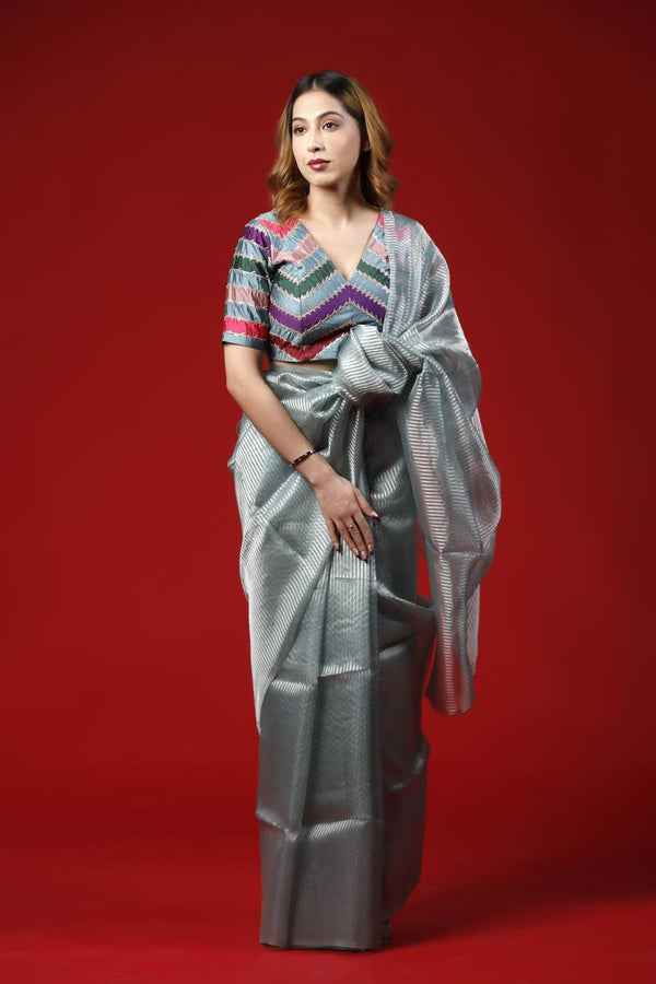 A woman wearing a blue-grey party wear saree dress for a cocktail party looks against a red background
