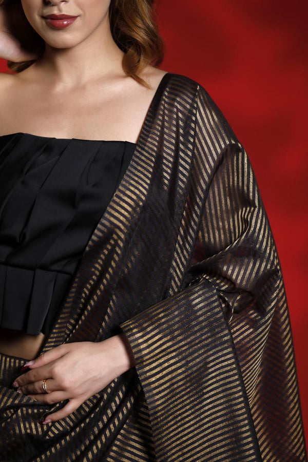 A woman wearing a black party wear saree with golden stripes against a red background