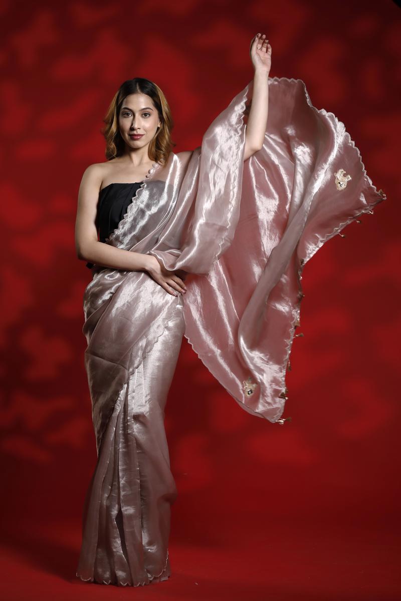 A woman wearing a light pink party wear saree with a red background