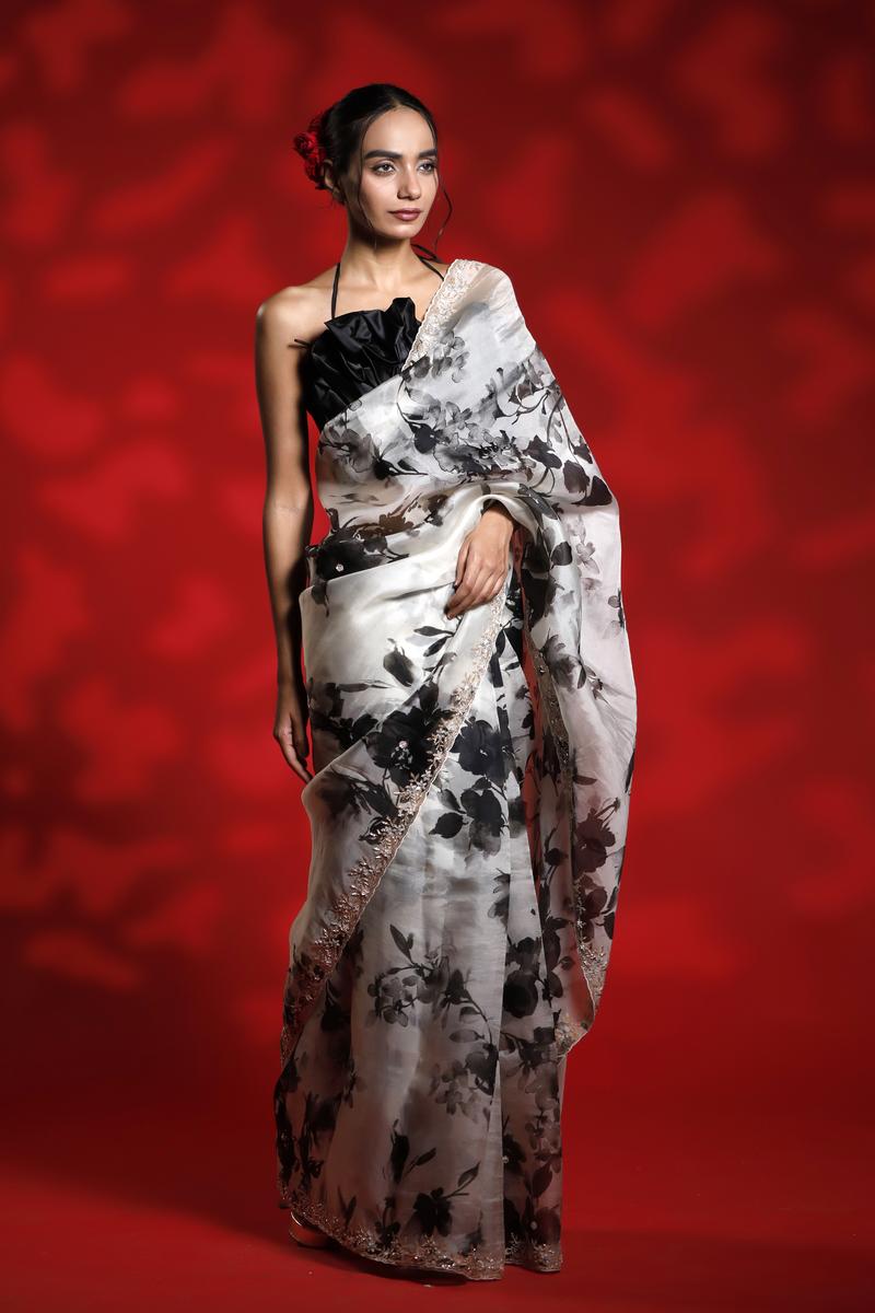 Woman wearing a floral party wear white saree dress for a cocktail party looks against a red background