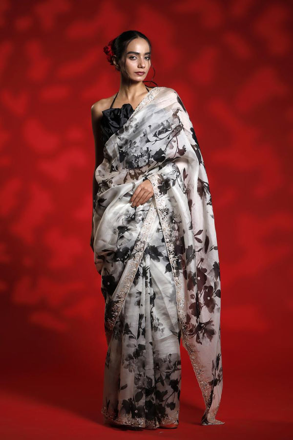 Woman wearing a floral party wear white saree dress for a cocktail party looks against a red background