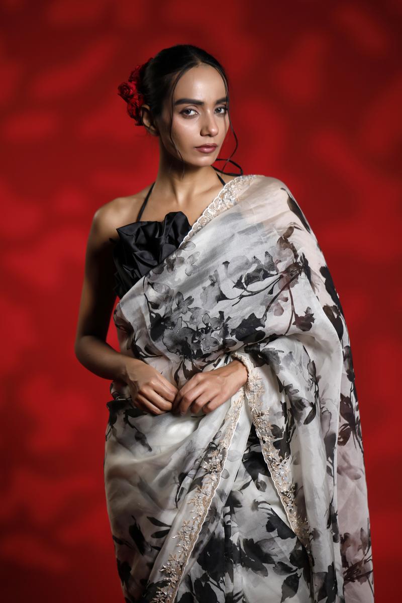 Woman wearing a floral party wear white saree dress for a cocktail party looks against a red background