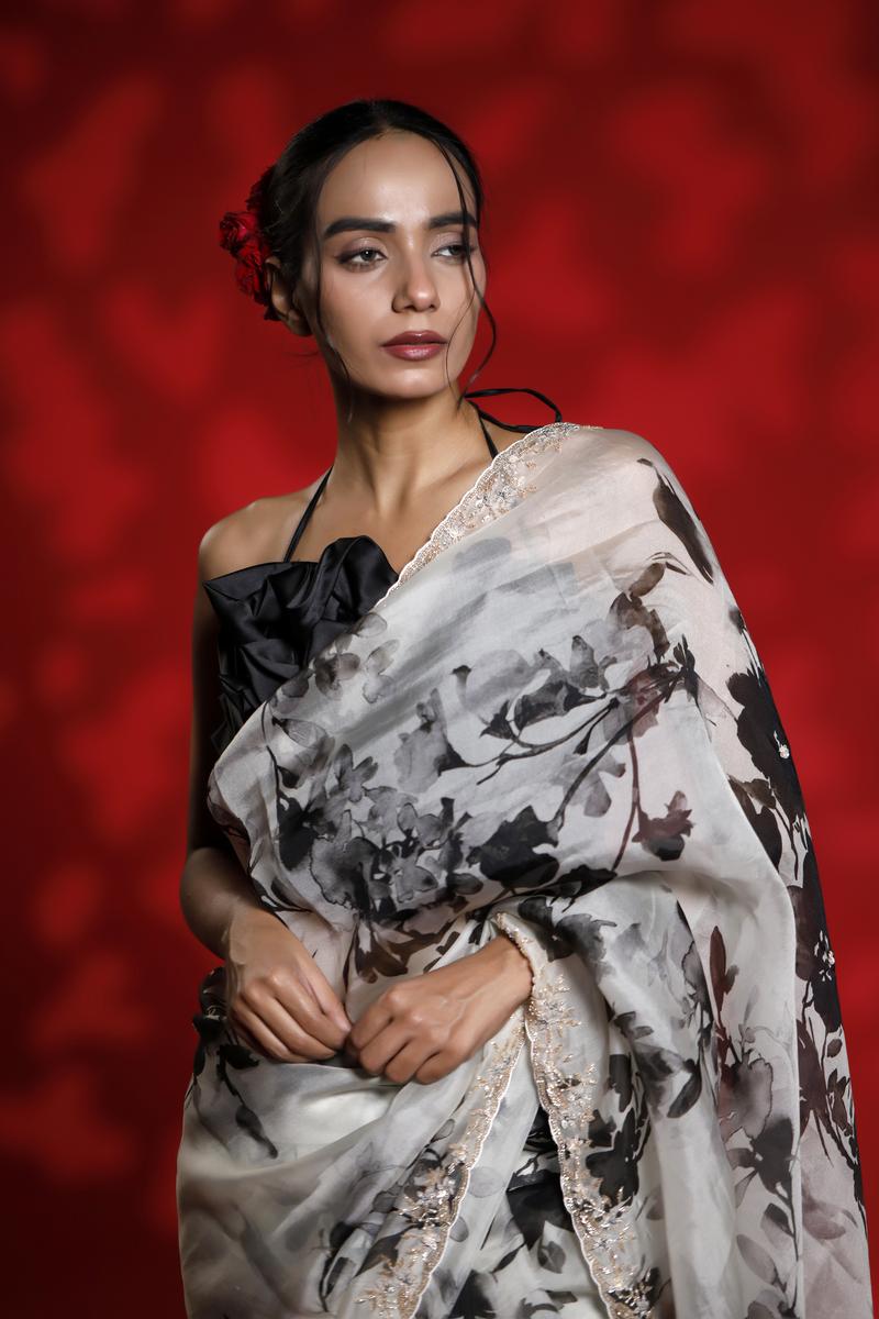 Woman wearing a floral party wear white saree dress for a cocktail party looks against a red background