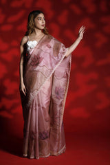 A woman wearing a mauve pink party wear saree with floral pichwai prints against a red background
