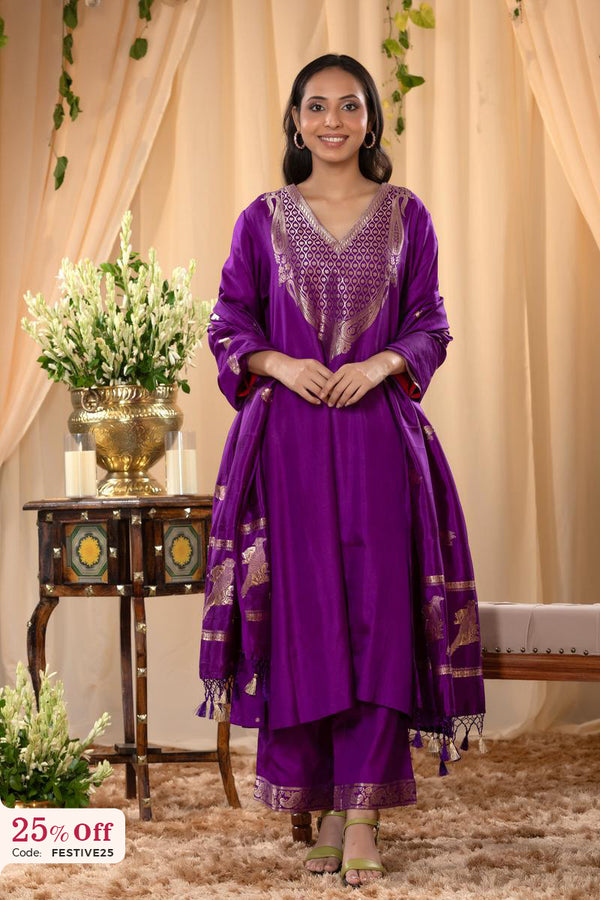 A woman in a traditional Diwali offer sale, purple salwar suit and purple banarasi dupatta is standing in a decorated room.