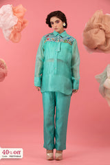 Woman wearing a teal outfit with floral embroidery on a pink background
