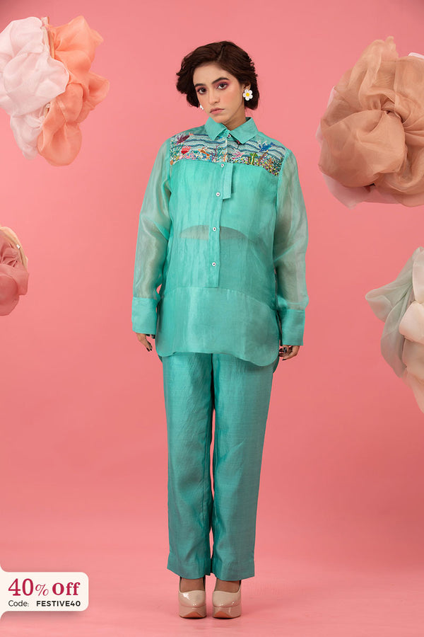 Woman wearing a teal outfit with floral embroidery on a pink background