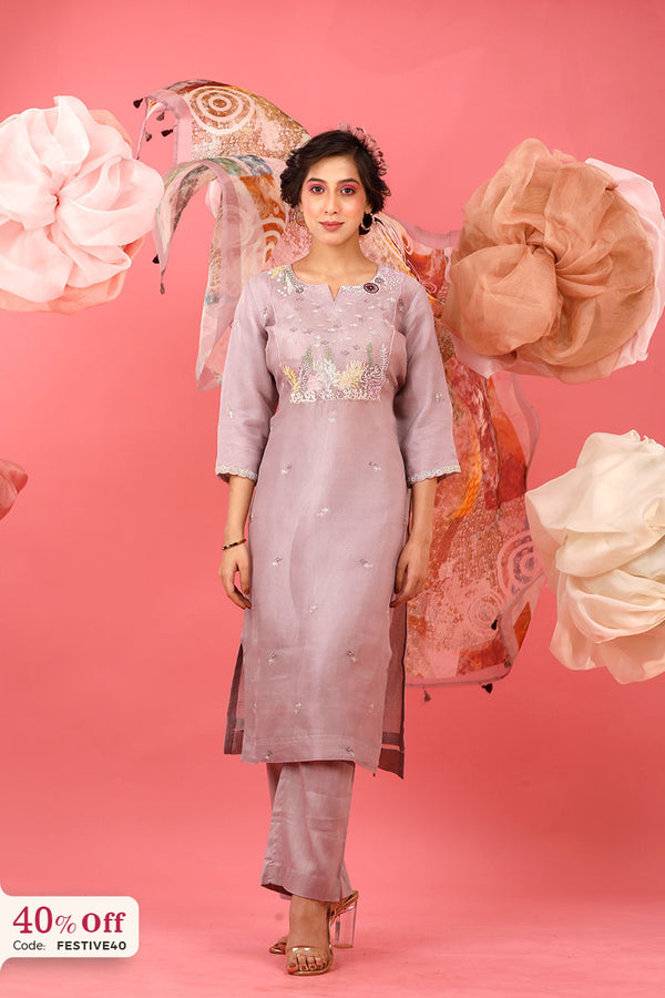 Woman in a pink traditional outfit with floral decorations on a pink background with promotional text.