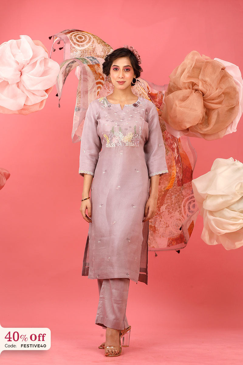 Woman in a pink traditional outfit with floral decorations on a pink background with promotional text.