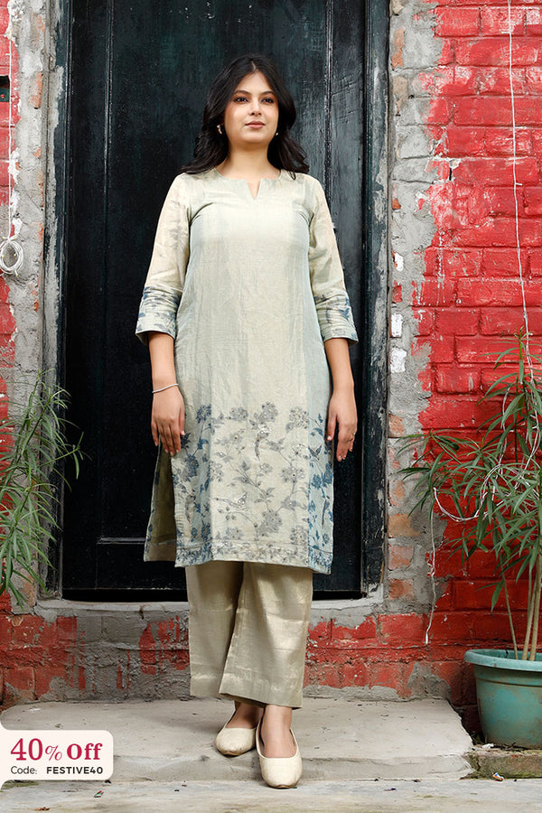 Woman wearing a light-colored kurta with pants standing in front of a red brick wall.