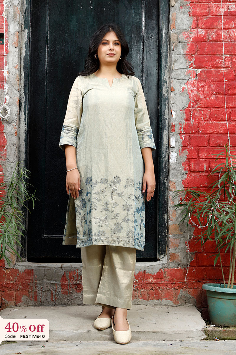 Woman wearing a light-colored kurta with pants standing in front of a red brick wall.