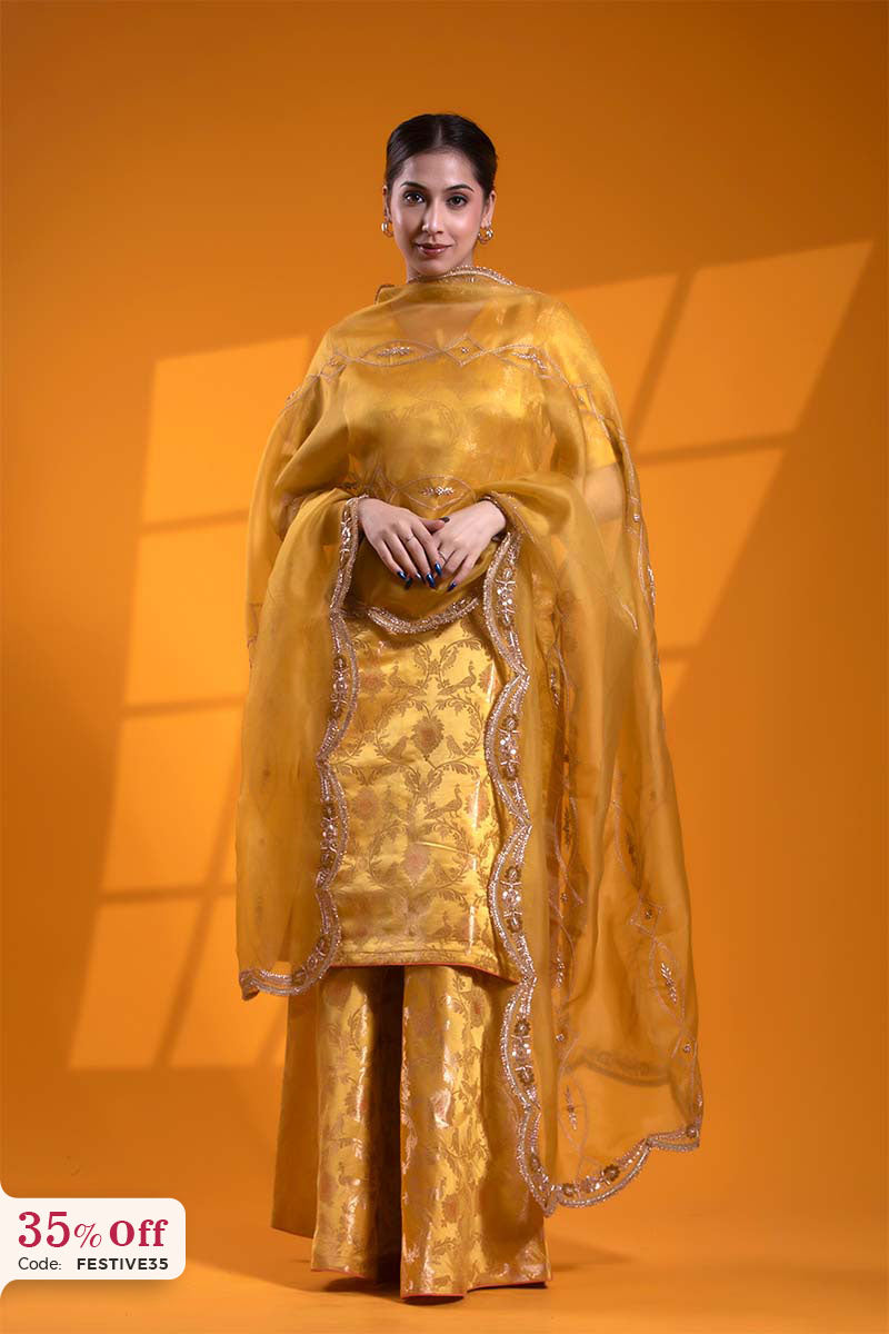 Woman wearing a yellow traditional outfit with a matching dupatta on an orange background