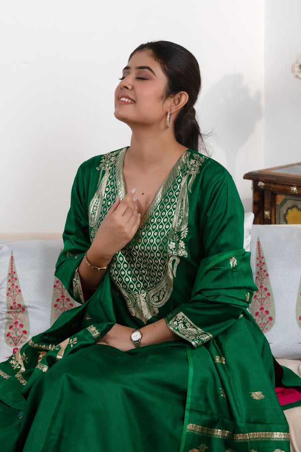 Woman wearing a green saree with gold patterns sitting on a couch.