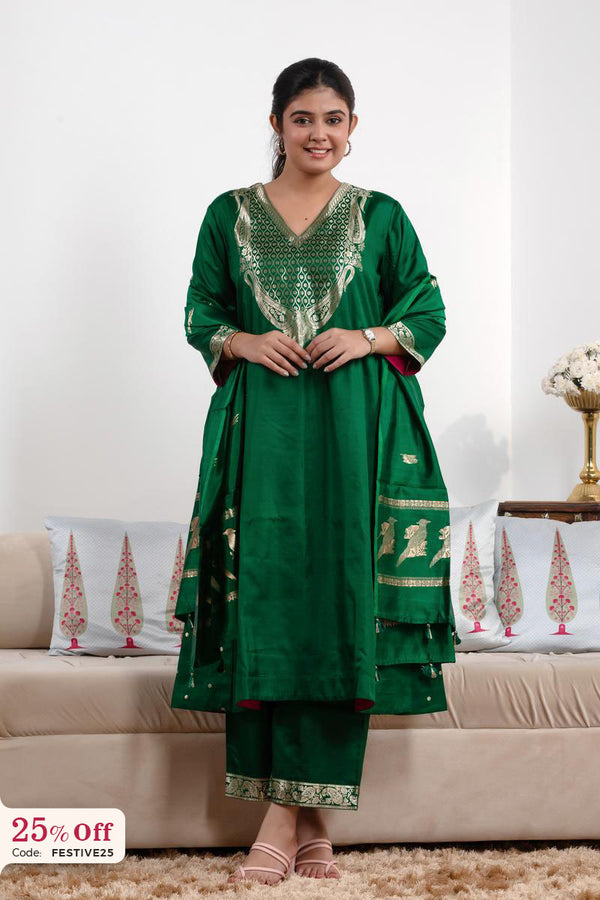 Woman wearing a green traditional outfit with gold embroidery in a living room setting.