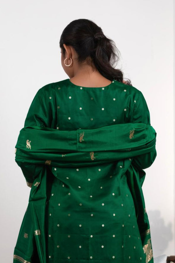 A woman wearing a green traditional outfit with a matching dupatta, standing against a white background.