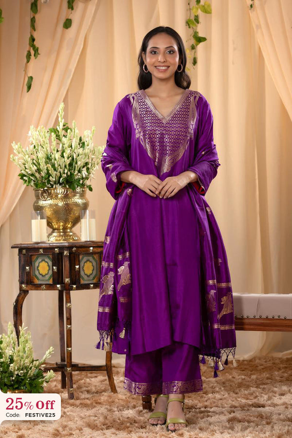 Woman in a purple traditional outfit standing in a decorated room with flowers and a table.