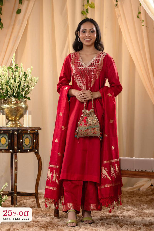 Woman in a red traditional outfit with gold details standing in front of beige curtains.