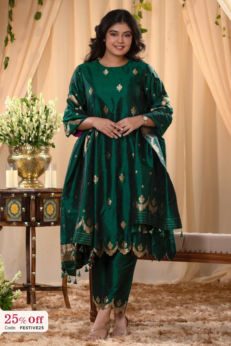 Woman wearing a green traditional outfit with gold patterns in a decorated room.