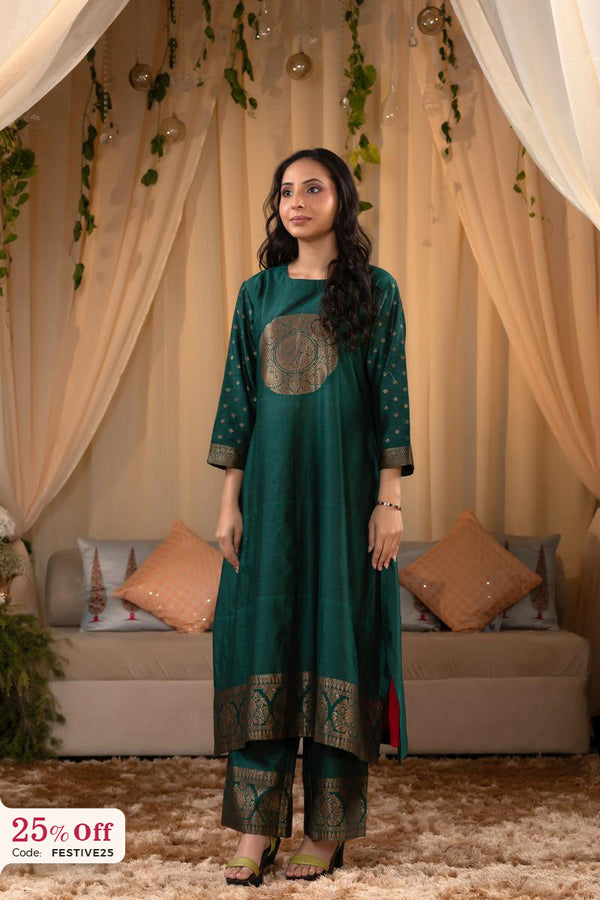 Woman in a green traditional outfit standing in a decorated room with beige curtains and pillows.