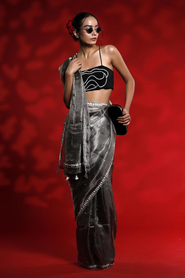 A woman wearing a silver grey party wear saree dress for a cocktail party looks against a red background