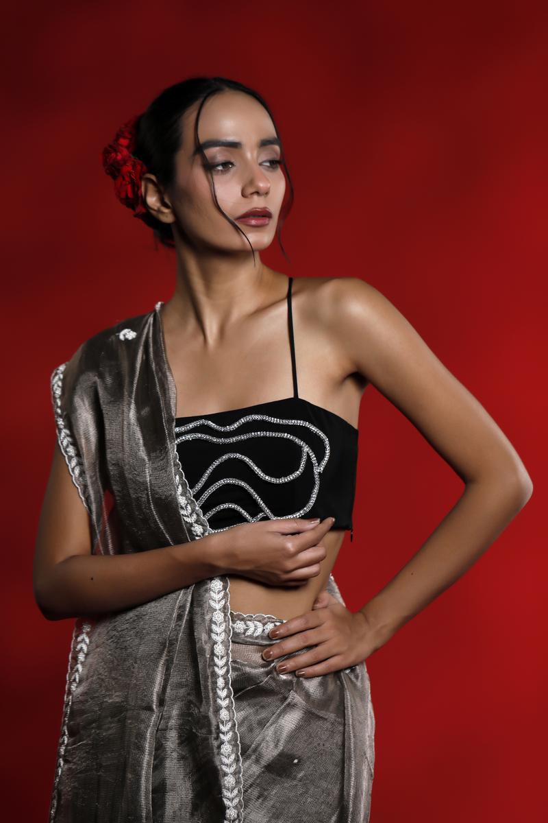 Woman wearing a black top with white patterns and a gray saree against a red background