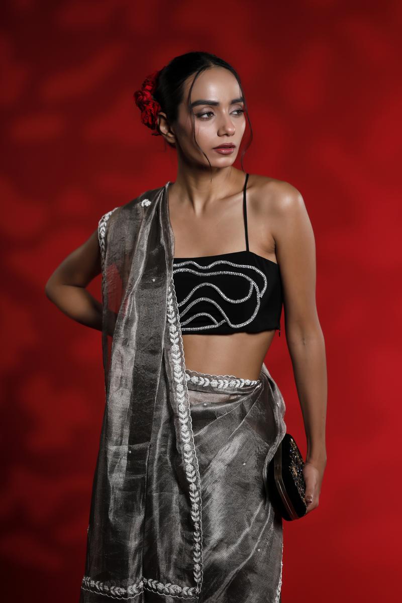 A woman wearing a silver grey party wear saree dress for a cocktail party looks against a red background