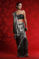 Woman wearing a black saree with silver border against a red background