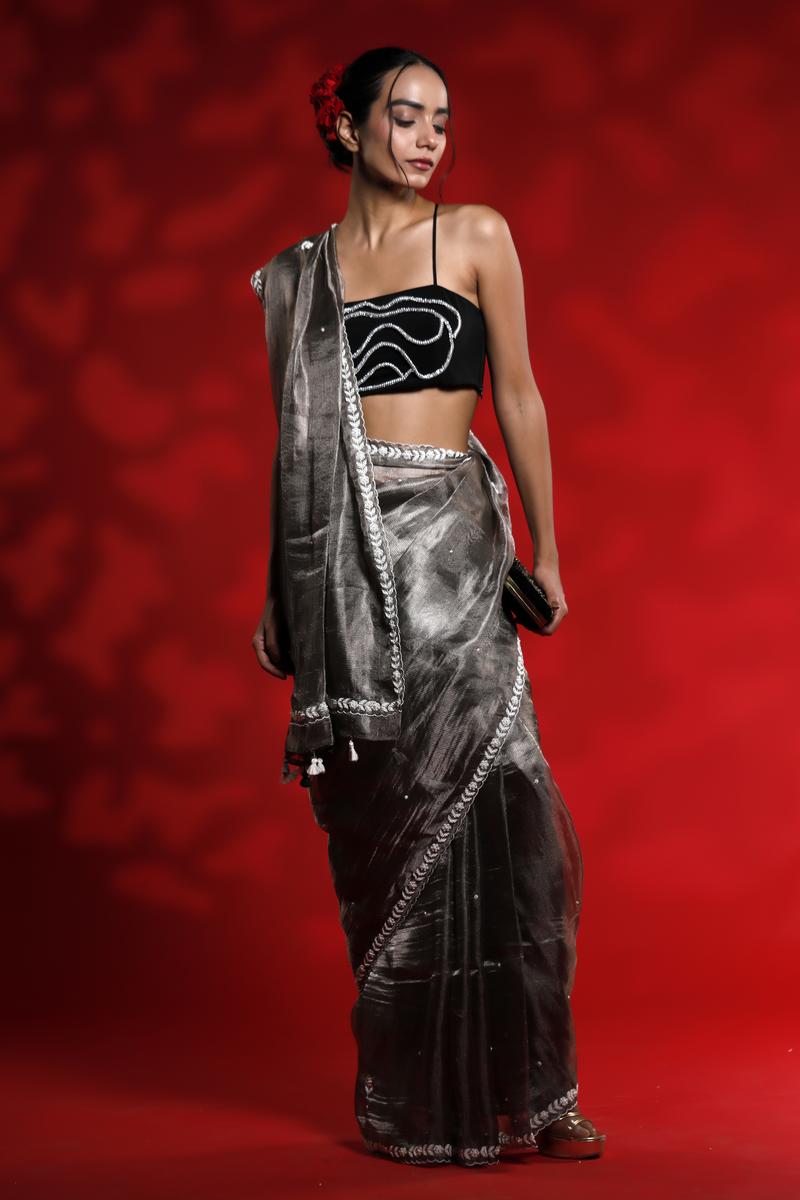 Woman wearing a black saree with silver border against a red background