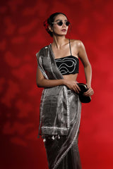 A woman wearing a silver grey party wear saree dress for a cocktail party looks against a red background