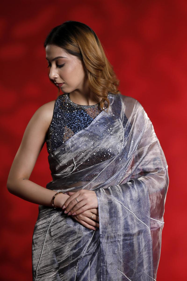 A woman wearing a shiny silver party wear saree with a red background