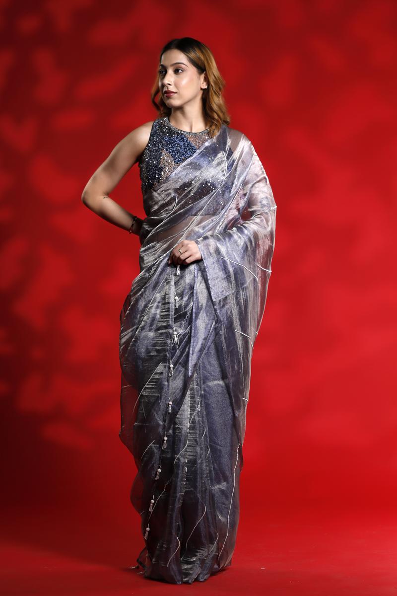 A woman wearing a shiny silver party wear saree with a red background