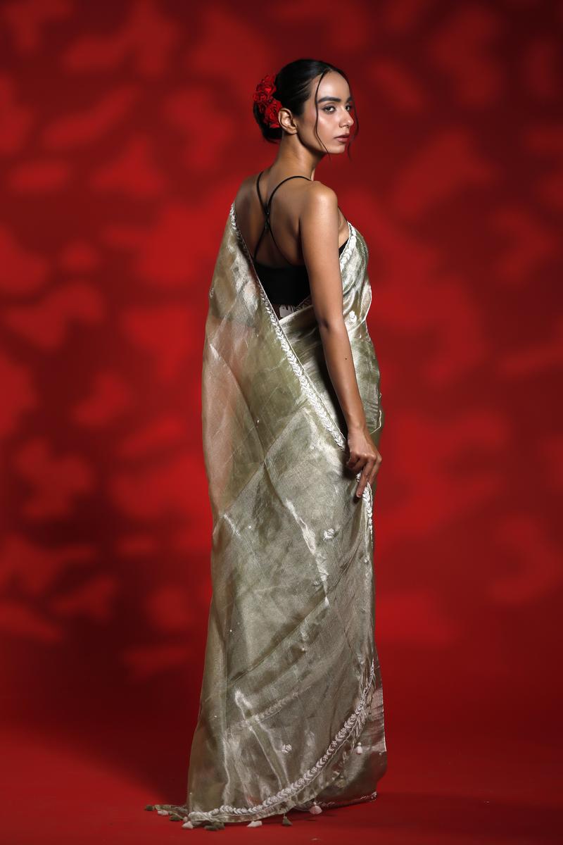 A woman wearing a shiny golden party wear saree with a red background, Tissue Silk Saree