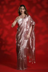 A woman wearing a pink party wear saree with a floral blouse against a red background