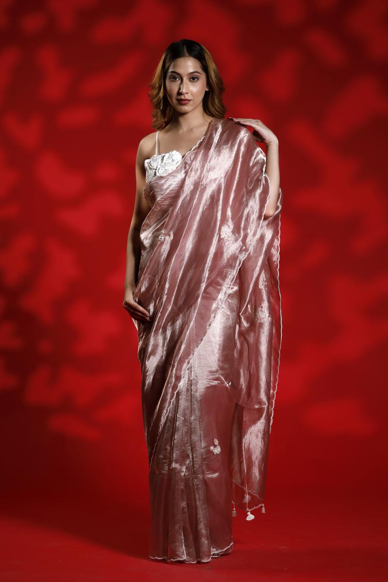 A woman wearing a pink party wear saree with a floral blouse against a red background
