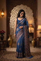 Woman in a blue tussar silk saree standing in an ornate room with decorative lamps and vases.