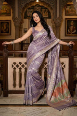 Woman wearing a Lilac Kadhwa Handloom Katan Silk Banarasi Saree with silver zari motifs and a Meenakari border, posing by a railing in a heritage setting with framed wall art.