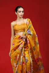 A woman wearing a mustard yellow party wear saree with floral prints against a red background